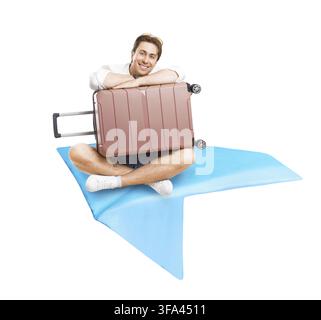 Smiling young man sitting on a huge blue paper airplane and hugging a pink suitcase. Creative concept for air travel, summer vacations and vacation tr Stock Photo