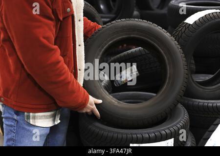 A customer holds a car tire while choosing new wheels in a car dealership with stacks of tires Stock Photo
