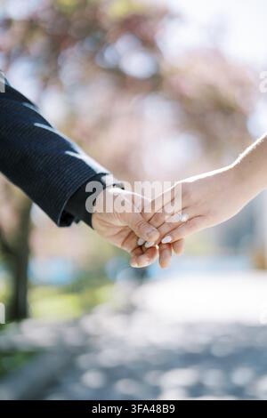 A close up of a couple holding hands outdoors, highlighting a sparkling diamond engagement ring on the woman's finger, with a soft blurred background Stock Photo