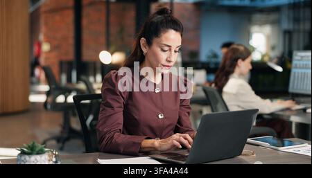 Finance, businesswoman and typing in office with laptop, data collection and payroll administration. Coworking, mature person and stats with computer Stock Photo