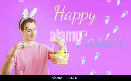 Cheerful man in bunny ears holding a blue Easter egg and a basket full of colorful eggs against a pink background with Happy Easter text and paw print Stock Photo