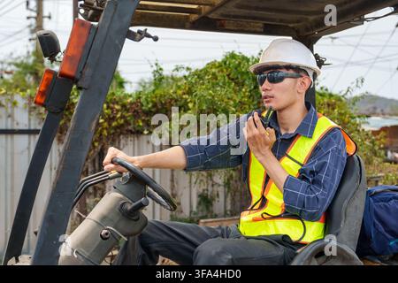 Construction worker driving a forklift while using a radio for effective communication on site. Ideal for concepts of safety, construction, and labor Stock Photo