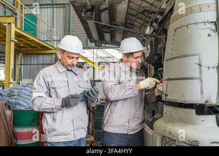 Two mechanics working on a truck engine in an industrial workshop for vehicle maintenance. Ideal for automotive, engineering, and mechanical service r Stock Photo