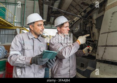 Two mechanics working on a truck engine in an industrial workshop for vehicle maintenance. Ideal for automotive, engineering, and mechanical service r Stock Photo
