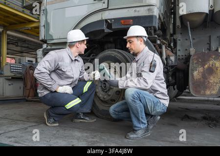 Two mechanics examining truck tire condition during routine maintenance at a workshop. Ideal for automotive, vehicle repair, and maintenance industry Stock Photo