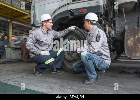 Two mechanics examining truck tire condition during routine maintenance at a workshop. Ideal for automotive, vehicle repair, and maintenance industry Stock Photo