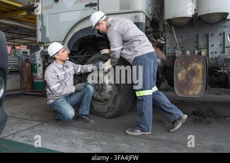 Two mechanics examining truck tire condition during routine maintenance at a workshop. Ideal for automotive, vehicle repair, and maintenance industry Stock Photo