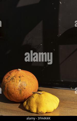 A pair of pumpkins in varying sizes sits on a wooden surface. The larger pumpkin, with mottled orange skin, contrasts against a smaller, yellow squash Stock Photo