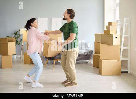 Happy couple dancing with moving boxes in new home, celebrating relocation teamwork Stock Photo