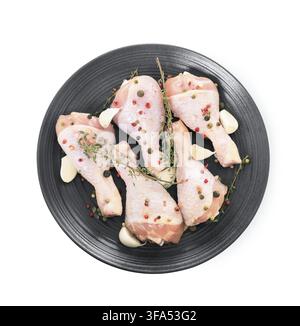 Raw chicken legs on black plate with thyme, garlic and peppercorns against white background Stock Photo