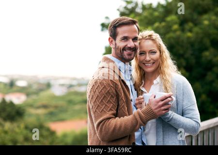 Portrait, coffee and couple on balcony in morning for bonding, connection and relax on weekend. Marriage, happy and man with woman with drink, hug and Stock Photo