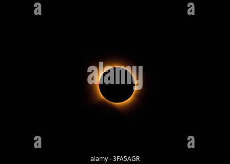 Total solar eclipse creating a dramatic celestial event with the moon obscuring the sun, revealing the glowing corona and a distinct red solar promine Stock Photo
