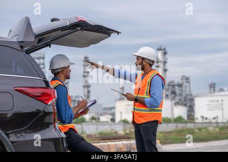 Engineers wearing safety gear including hard hats examining survey tablet standing industrial facility. Stock Photo