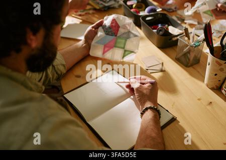Man Sketching Design in Notebook during Creative Sewing Workshop Stock Photo