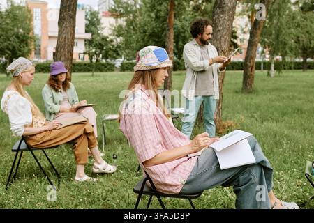 Diverse Group of People Drawing in Sketchbooks during Outdoor Art Class Stock Photo