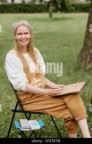 Portrait of Smiling Woman Drawing in Sketchbook during Outdoor Art Class Stock Photo