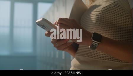 Female Educator Using Smartphone In School Locker Room After Students Have Left. Concept Of Mobile Productivity, Instant Communication, Educational Teamwork, Connected Professionals In Digital Age. Stock Photo