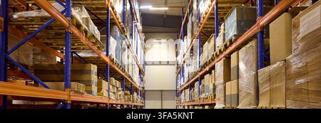 Long aisle in storage warehouse with shelves, pallets and boxes stacked neatly Stock Photo