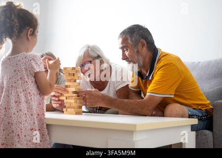 Happy grandparents playing wooden block tower game with their granddaughters at home Stock Photo