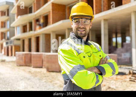 Happy contractor in safety glasses looking aside with crossed arms Stock Photo