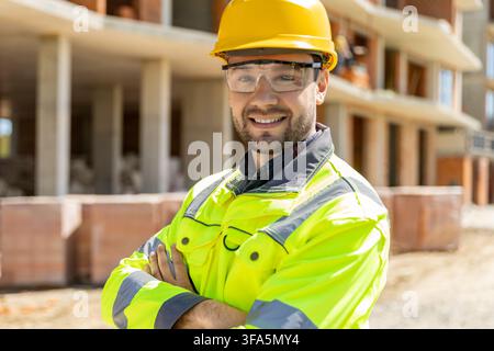 Smiling engineer wearing yellow helmet standing with arms crossed Stock Photo