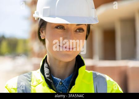 Professional female builder wearing protective hard hat looking away Stock Photo