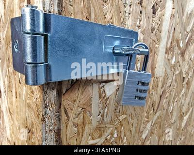Heavy-duty stainless steel swivel safety hasp and staple latch paired with a 3-digit combination padlock, installed on an oriented strand board (OSB) Stock Photo