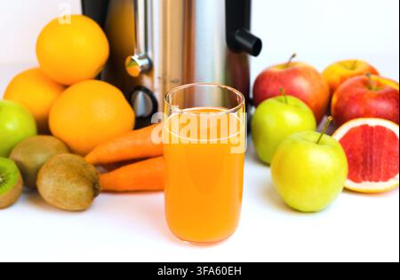 A glass of freshly squeezed fruit juice, fruit and a modern juicer on the table in the kitchen. Homemade healthy fruit and vegetable juices. Selective Stock Photo