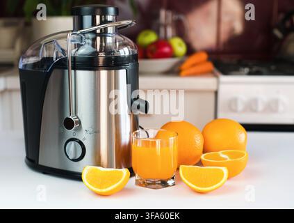 Modern juicer, glass of fresh orange juice and oranges on the table in the kitchen. Natural and healthy juices. Close-up. Stock Photo