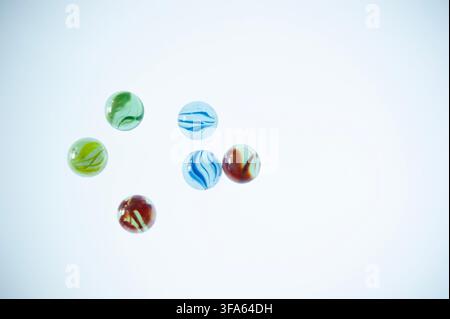 ix colorful glass marbles scattered on a clean white background with generous copy space, viewed from above Stock Photo