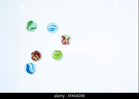 ix colorful glass marbles scattered on a clean white background with generous copy space, viewed from above Stock Photo