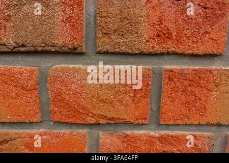 Close-up of a weathered red brick wall showing varied orange-red tones, rough masonry texture and grey mortar joints Stock Photo
