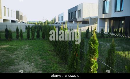 Modern townhouses reflecting urban development and suburban living, featuring green landscaping along a fence Stock Photo