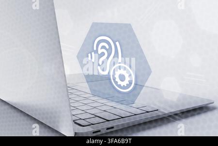 A sleek laptop displays a glowing icon of an ear and gear, representing advanced digital accessibility technology and hearing assistance solutions. Stock Photo