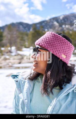 Black Woman Hiking in a Snowy Forest admiring the nature landscape cheerfully. Stock Photo