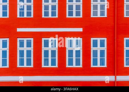 A striking architectural detail featuring a bright red brick wall with evenly spaced white-paned windows and horizontal white bands. Copenhagen Stock Photo