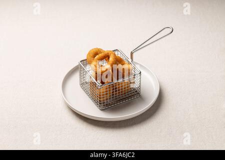 Crispy golden onion rings served in a small metal basket on a white plate. Minimalistic styling and soft light highlight texture and warmth, ideal for Stock Photo