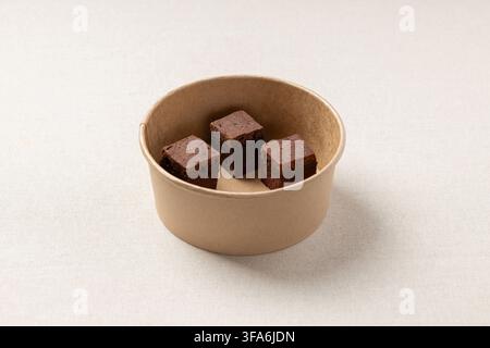 Three pieces of chocolate brownie arranged in a brown paper bowl. The natural light and simple setup emphasize texture, eco-friendly packaging, and co Stock Photo