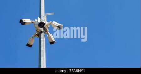 Multiple security cameras mounted on a pole against clear blue sky, symbolizing security, monitoring, and urban safety. Stock Photo