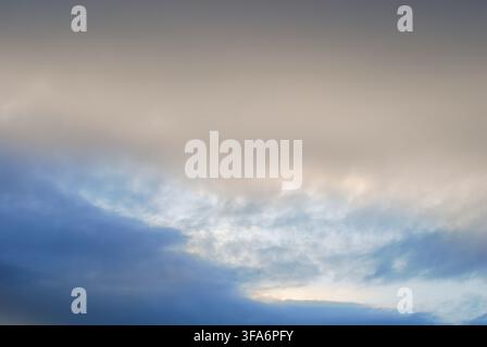Beautiful atmospheric cloudscape showing a dramatic contrast between thick grey storm clouds above and a bright blue sky with soft light breaks below Stock Photo