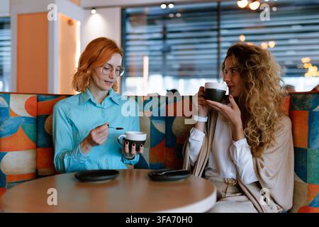 Engaging conversation between two businesswomen enjoying coffee in a modern cafe during a productive afternoon meeting Stock Photo
