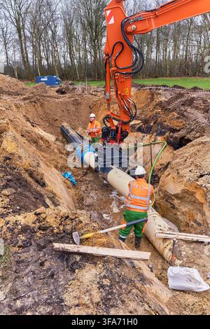 Water pipeline construction in Hoogeveen, Netherlands, with crane and workers installing transition coupling between PE and PVC pipes Stock Photo