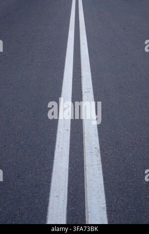 Vertical view of double solid white lines painted on a dark asphalt road. Concept of traffic separation, road safety regulations, lane division, and h Stock Photo