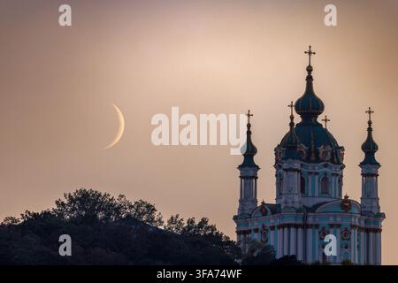Young crescent Moon beside St. Andrew's Church in Kyiv, Ukraine, photographed at dusk on August 16, 2026 Stock Photo