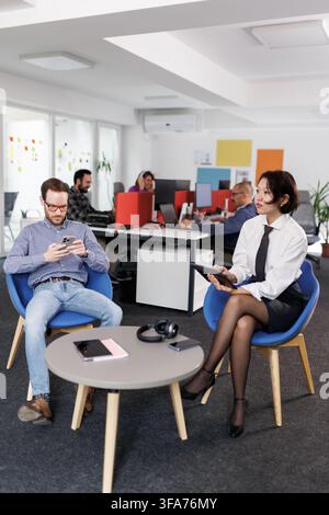 Businesspeople engaged in conversation and multitasking inside a modern office space during working hours Stock Photo