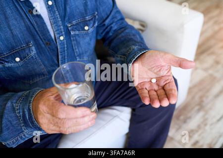 Senior man self medicating at home, elderly care and independence, taking daily prescription medicine with water. Patient managing health and wellness Stock Photo