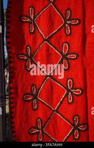 Detailed texture of a bright red felted wool textile decorated with dark embroidered geometric floral diamonds. Stock Photo