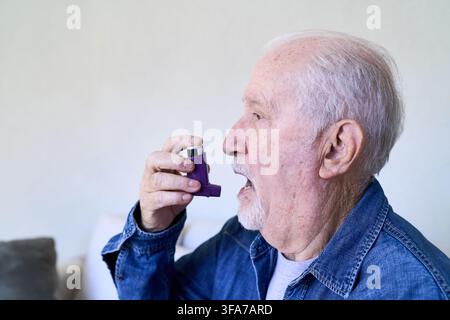 Senior man using an asthma inhaler for self medication, home healthcare and elderly care concepts. Respiratory health and independence in old age, a p Stock Photo