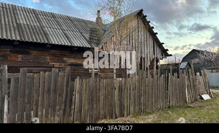 Old dilapidated log house behind a broken wooden fence, abandoned rural building in ruins. High quality photo Stock Photo