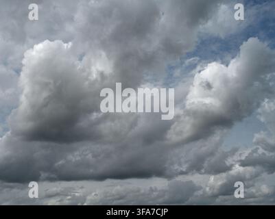 Horizontal close up of a mostly cloudy sky with white clouds showing shadows and highlights and small blue patches that darken toward the top Stock Photo